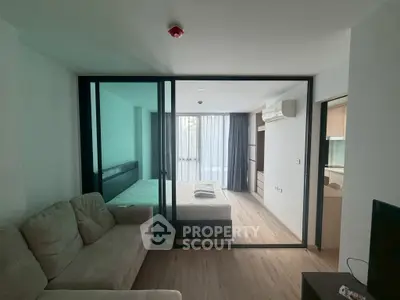 Modern studio apartment with glass partition, cozy sofa, and natural light.