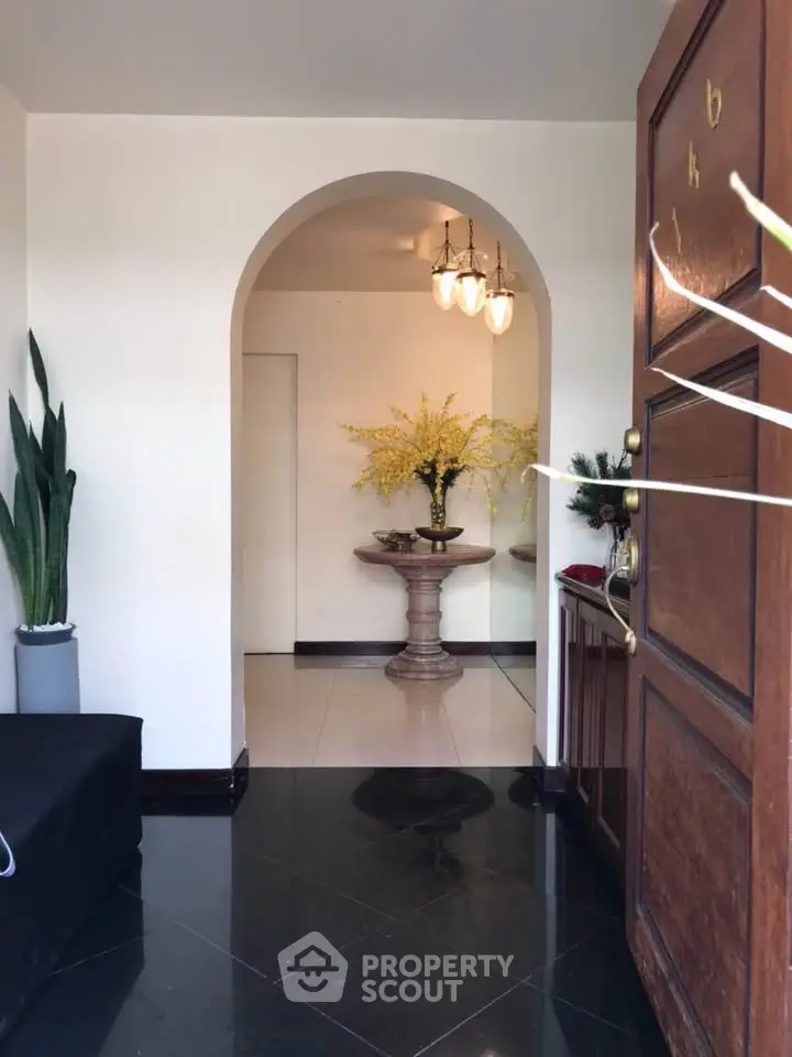 Elegant entrance with polished black floor and decorative plants, leading to a stylish interior with a classic pedestal table.