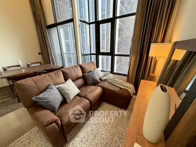 Spacious living room with large windows and cozy brown sofa in modern apartment.