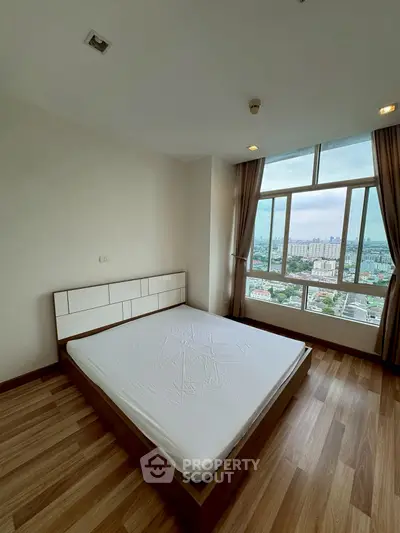 Spacious bedroom with large window offering stunning city view and natural light.