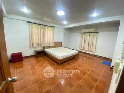 Spacious bedroom with wooden flooring and natural light, featuring a comfortable bed and air conditioning.