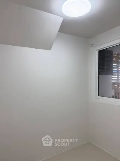 Minimalist small room with window and ceiling light, ideal for storage or compact office space.