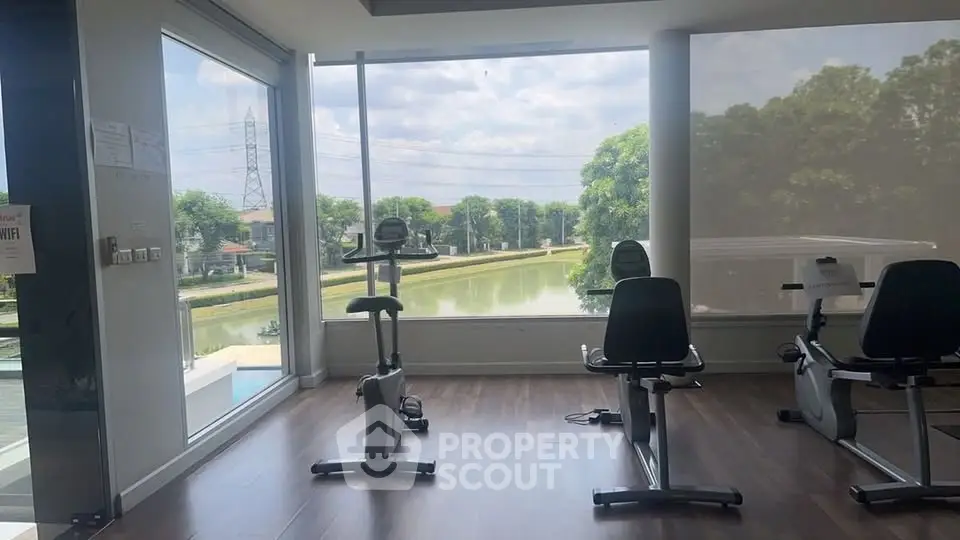 Modern gym with large windows offering scenic river views and state-of-the-art exercise equipment.