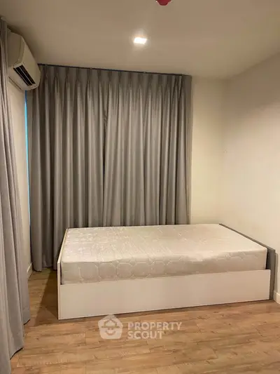 Cozy bedroom with minimalist design and wooden flooring, featuring a single bed and elegant curtains.