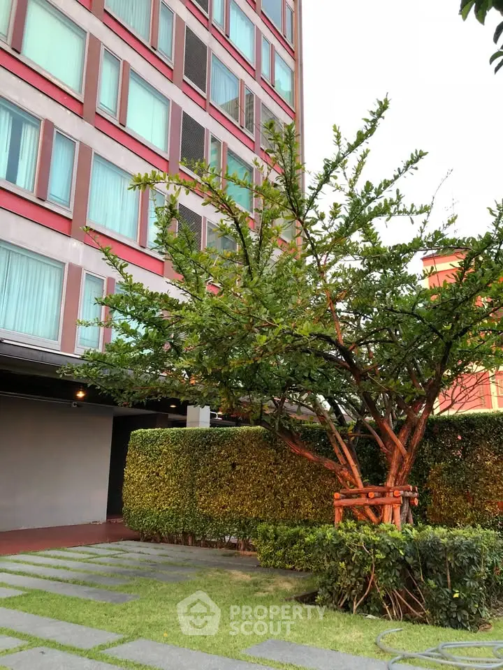 Modern building exterior with lush garden and tree, showcasing urban greenery.
