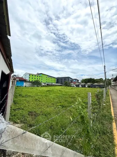 Spacious green plot with potential for development, surrounded by modern buildings and clear skies.