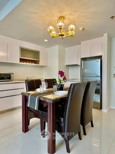 Modern kitchen with dining area, sleek cabinets, and elegant chandelier lighting.