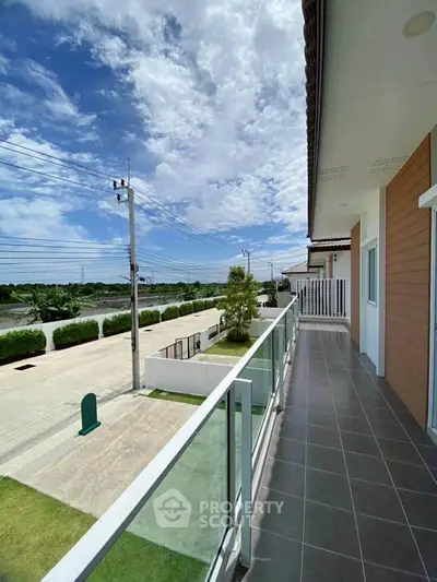 Spacious balcony with glass railing offering scenic views of the neighborhood and blue skies.