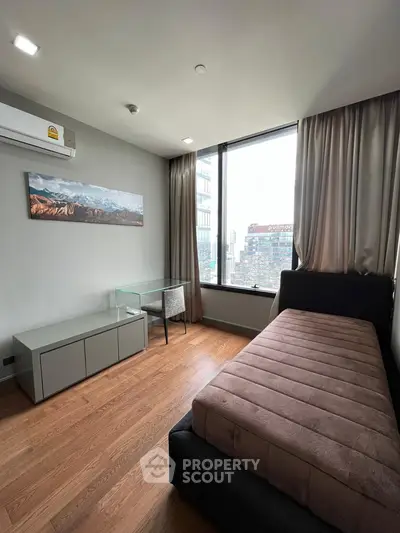 Modern bedroom with city view, featuring sleek furniture and large window for natural light.