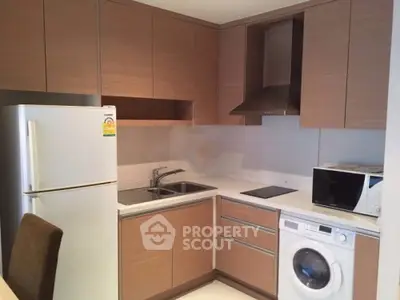 Modern kitchen with wooden cabinets, fridge, washing machine, and microwave in a compact layout.