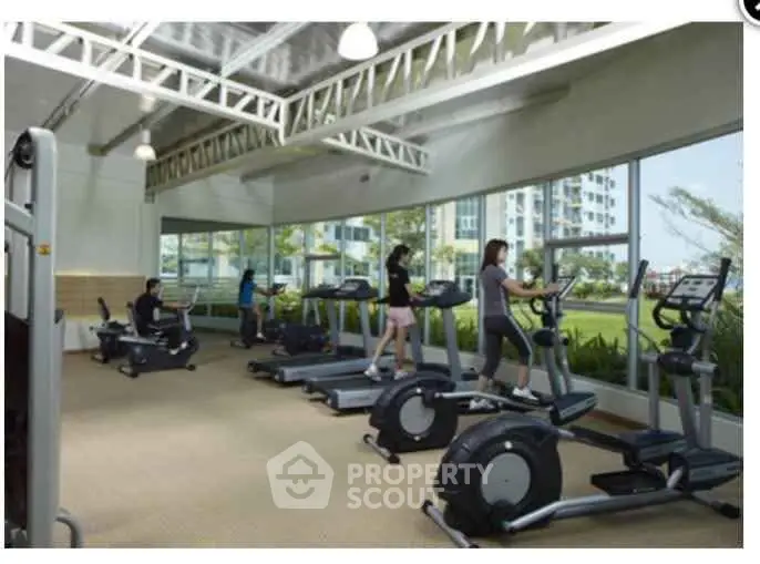Modern gym with cardio equipment and large windows in a residential complex.