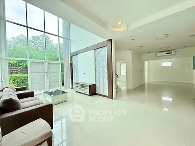Spacious modern living room with high ceilings and large windows offering natural light and garden view.