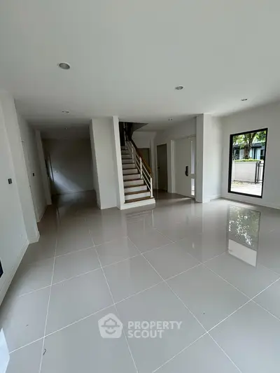 Spacious modern living area with glossy tiled floors and staircase, perfect for family gatherings.