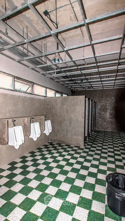 Spacious public restroom with urinals and stalls, featuring checkered flooring and industrial ceiling.