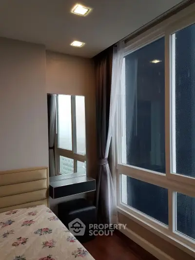 Modern bedroom with large windows offering city view, featuring elegant decor and natural light.