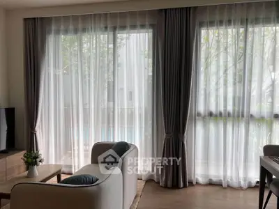 Elegant living room with large windows and sheer curtains, offering a serene garden view.