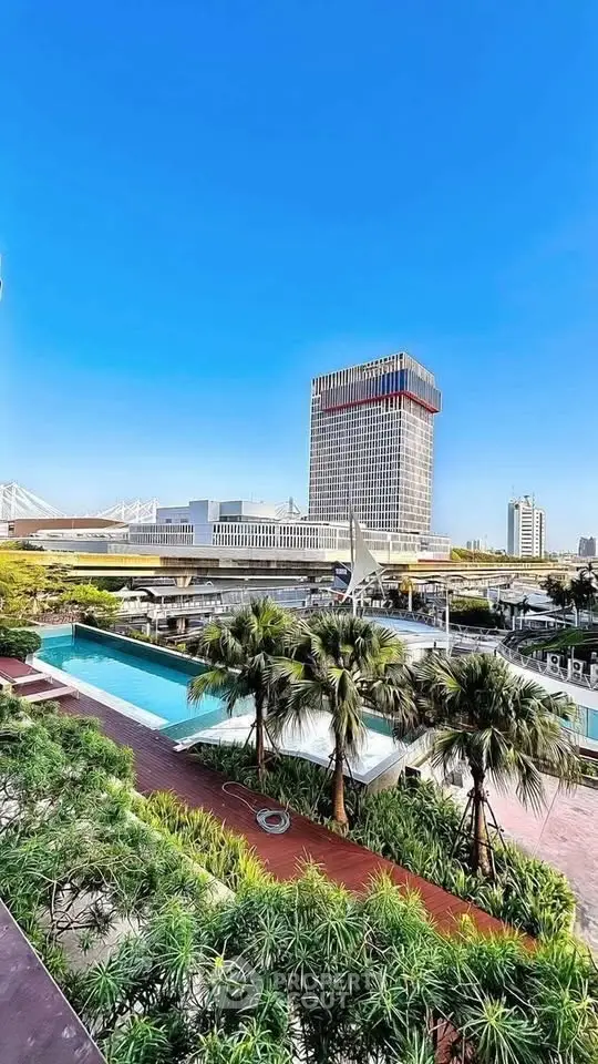 Stunning cityscape view with modern building and luxurious pool surrounded by lush greenery.