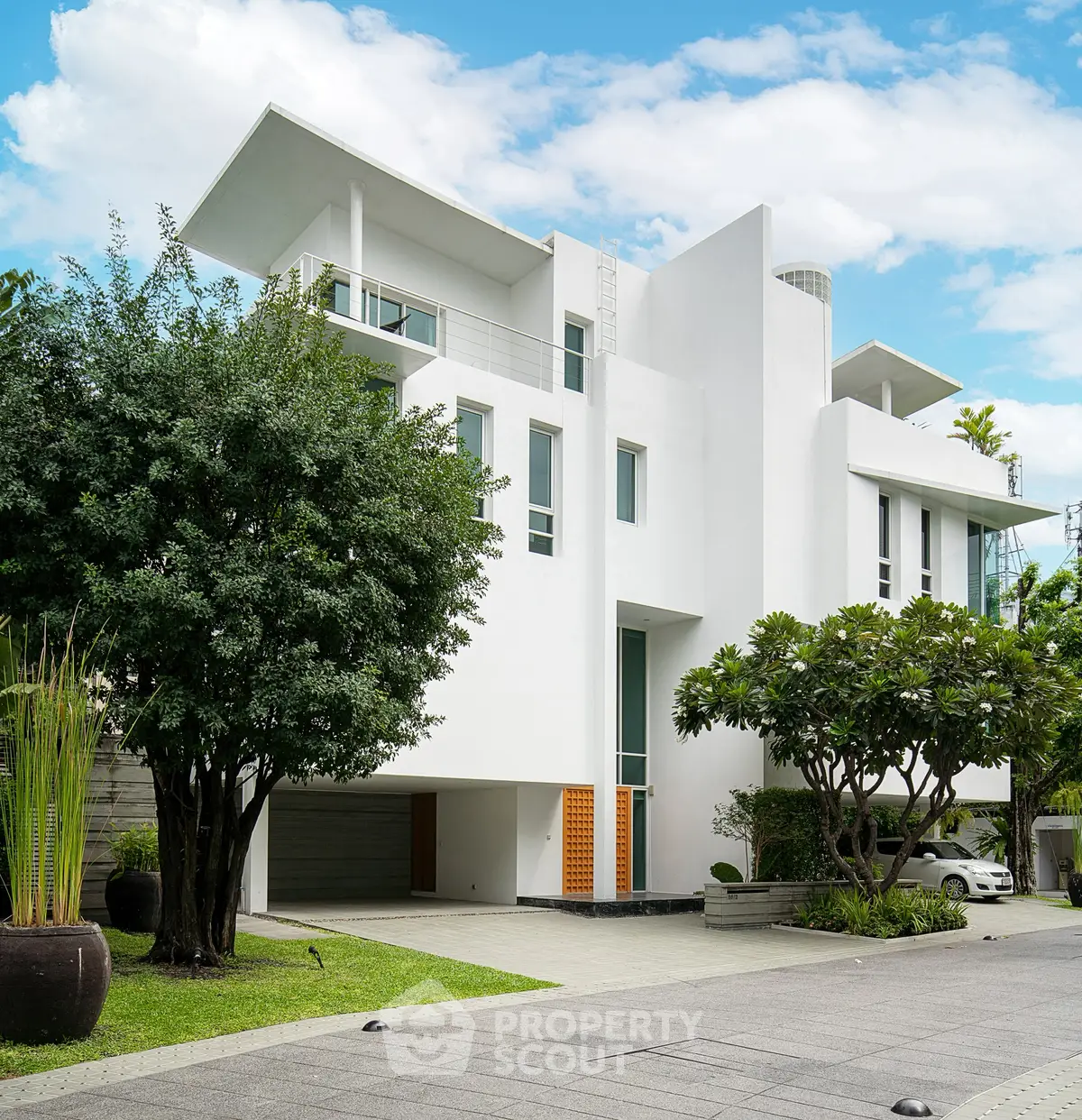 Modern white multi-story house with lush greenery and spacious driveway