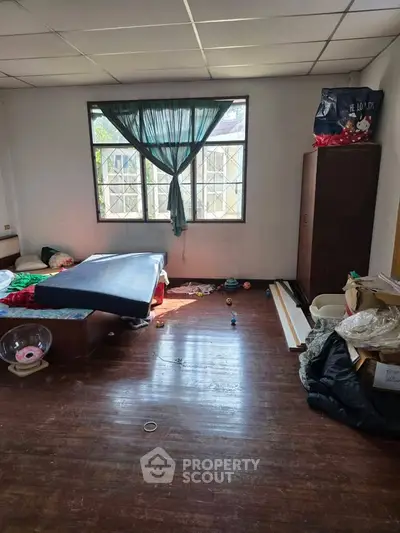 Spacious bedroom with large window and wooden flooring, ideal for renovation and personalization.