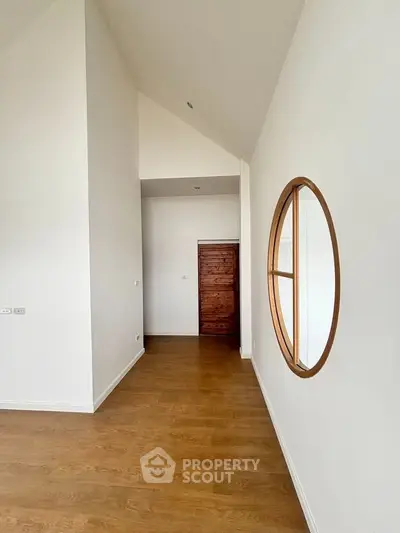 Spacious hallway with wooden flooring and unique circular window design.