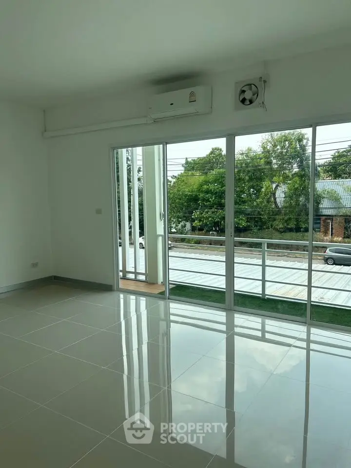 Spacious living room with large windows and balcony access, offering a serene view of greenery.
