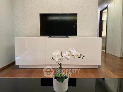 Modern living room with sleek TV stand and elegant orchid centerpiece on wooden floor.