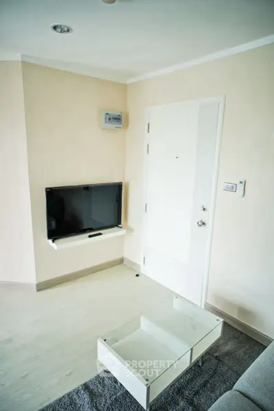 Modern minimalist living room with wall-mounted TV and sleek glass coffee table.