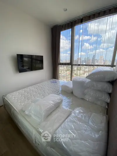 Modern bedroom with large windows offering stunning city views, featuring a wall-mounted TV and cozy bedding.