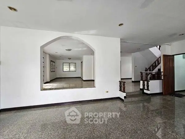 Spacious open-plan living area with elegant staircase and large windows.