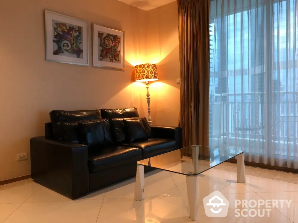 Elegant living room with leather sofa and glass coffee table, featuring modern art and warm lighting.