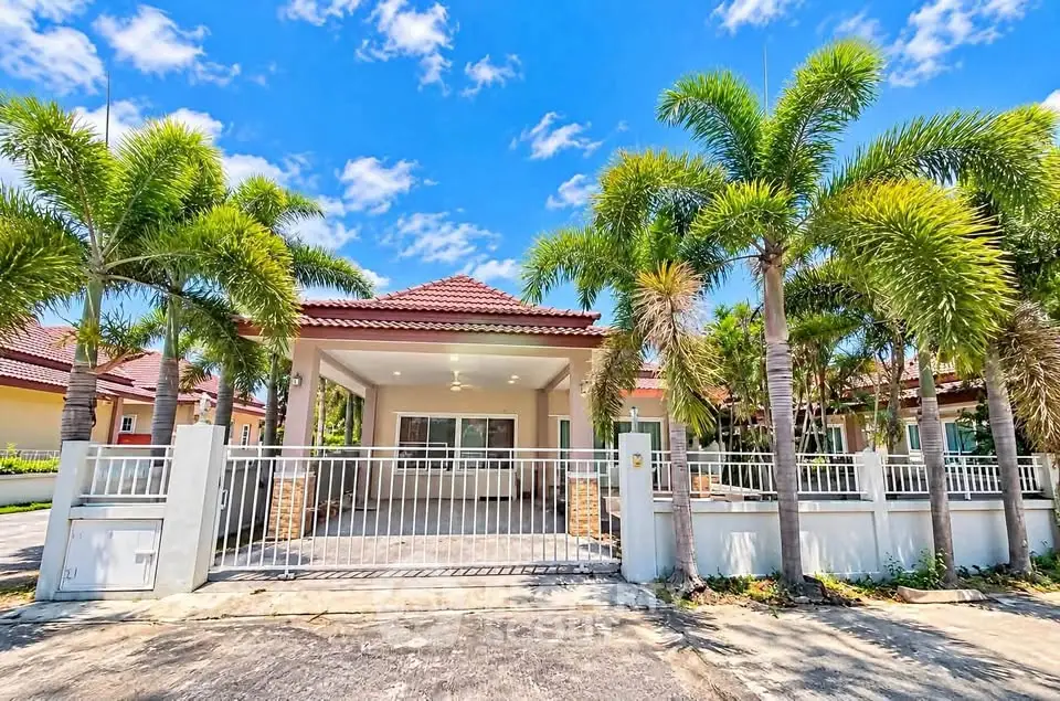 Charming tropical villa with palm trees and gated entrance under a bright blue sky.