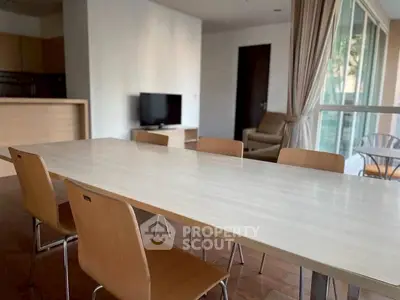 Spacious dining area with modern wooden table and chairs, adjacent to a cozy living room with natural light.
