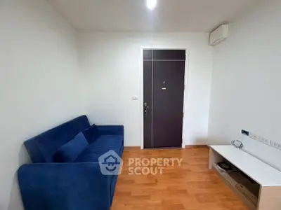 Modern living room with blue sofa and wooden flooring, featuring a sleek entrance door.