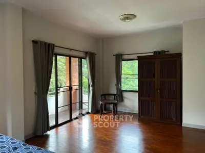 Spacious bedroom with balcony access and wooden flooring in serene setting.