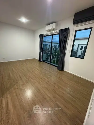 Spacious empty room with wooden flooring and large windows offering a view, perfect for customization.