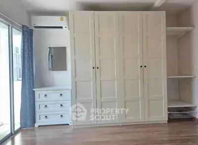Spacious bedroom with large wardrobe and elegant dresser, featuring natural light from sliding glass doors.