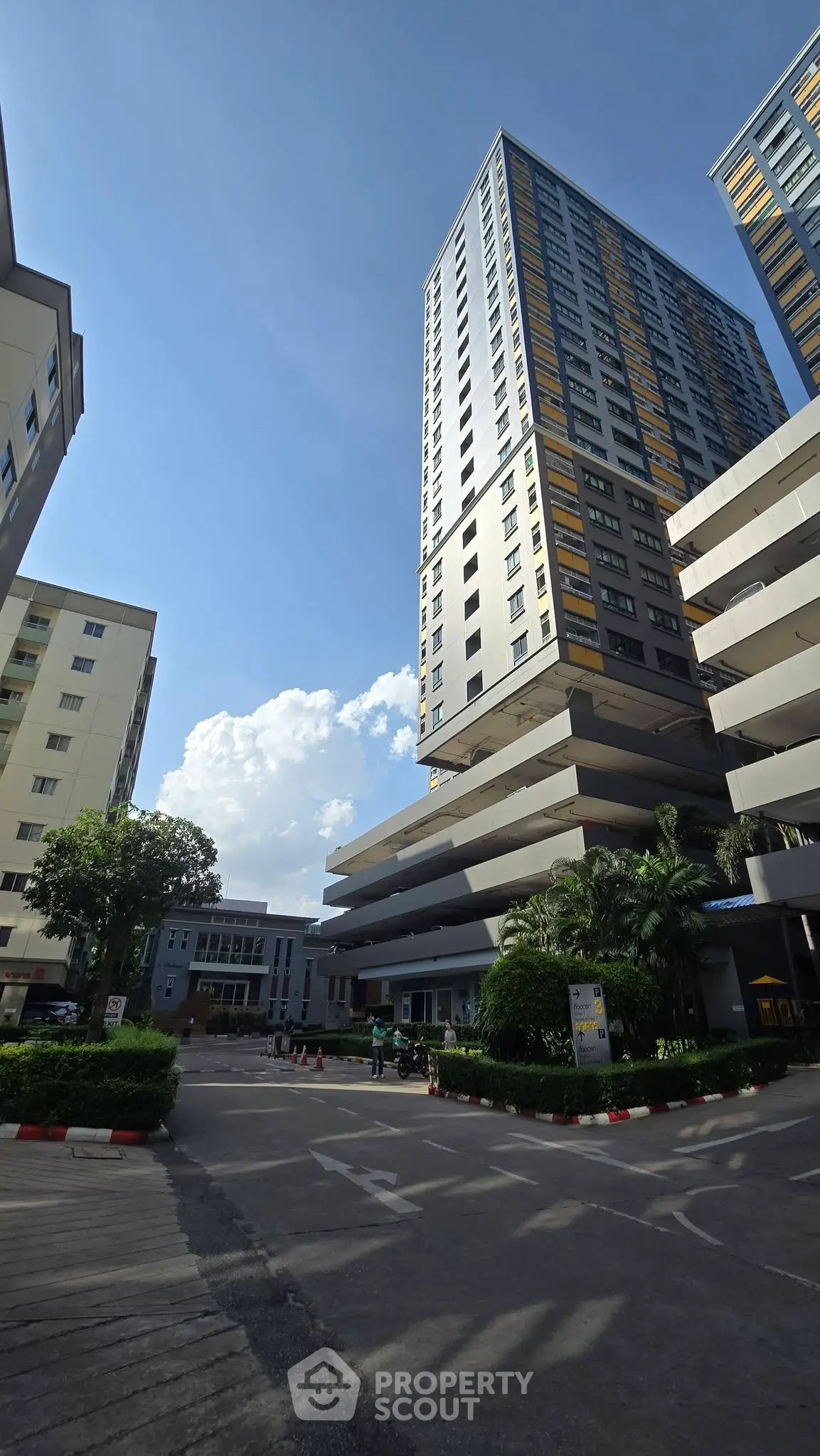 Modern high-rise residential building with lush landscaping and clear blue sky.