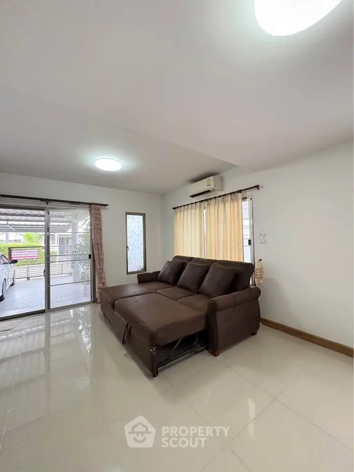 Spacious living room with large windows and modern brown sofa, perfect for relaxation and entertaining.