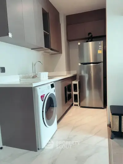 Modern kitchen with sleek cabinets, washing machine, and stainless steel fridge in compact layout.