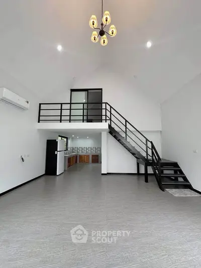 Spacious modern living room with high ceiling and loft, featuring sleek staircase and open kitchen layout.