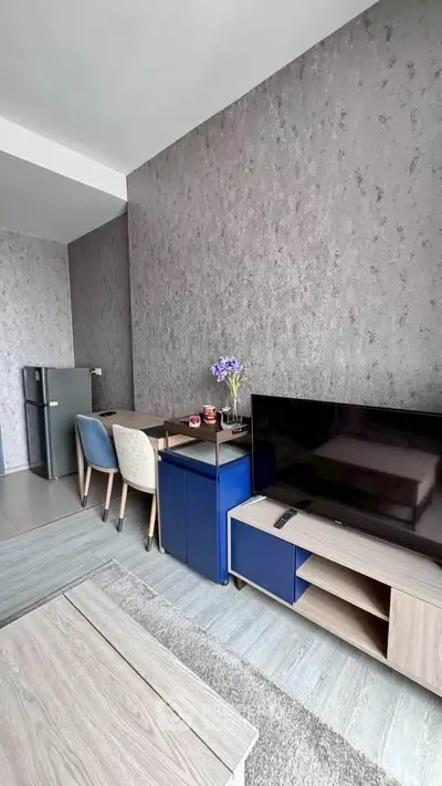 Modern living room with stylish decor, featuring a TV, dining area, and sleek refrigerator.