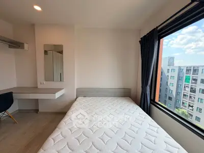 Modern bedroom with large window and city view, featuring a comfortable bed and sleek workspace.