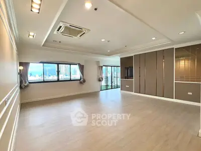 Spacious modern living room with large windows and city view, featuring elegant ceiling design and wooden flooring.