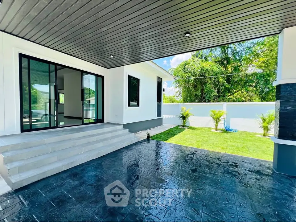 Modern home exterior with sleek black and white design, spacious patio, and lush green garden.