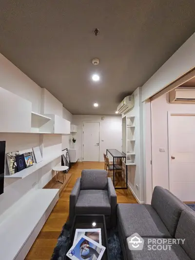 Modern minimalist living room with sleek white shelving units, cozy grey sofas, and warm wooden flooring, perfect for urban living.