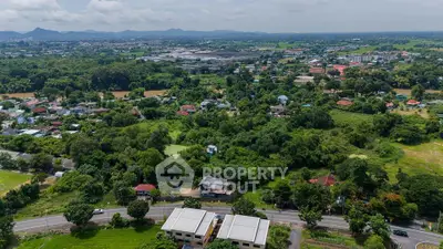 Aerial view of lush green landscape with residential area and distant mountains.