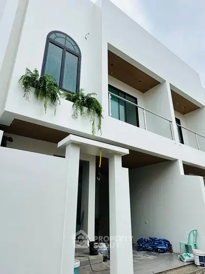 Modern two-story white building with large windows and balcony, featuring sleek architectural design.