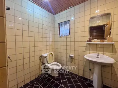 Charming vintage bathroom with tiled walls and wooden ceiling, featuring a classic pedestal sink and toilet.