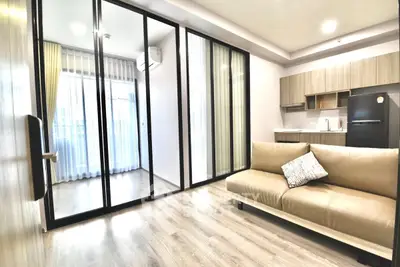 Modern living room with open kitchen and large glass doors leading to balcony.