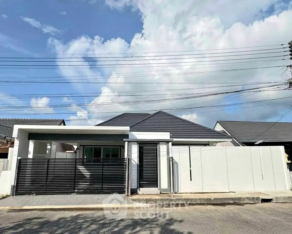 Modern single-story house with sleek design and gated entrance under a clear blue sky.
